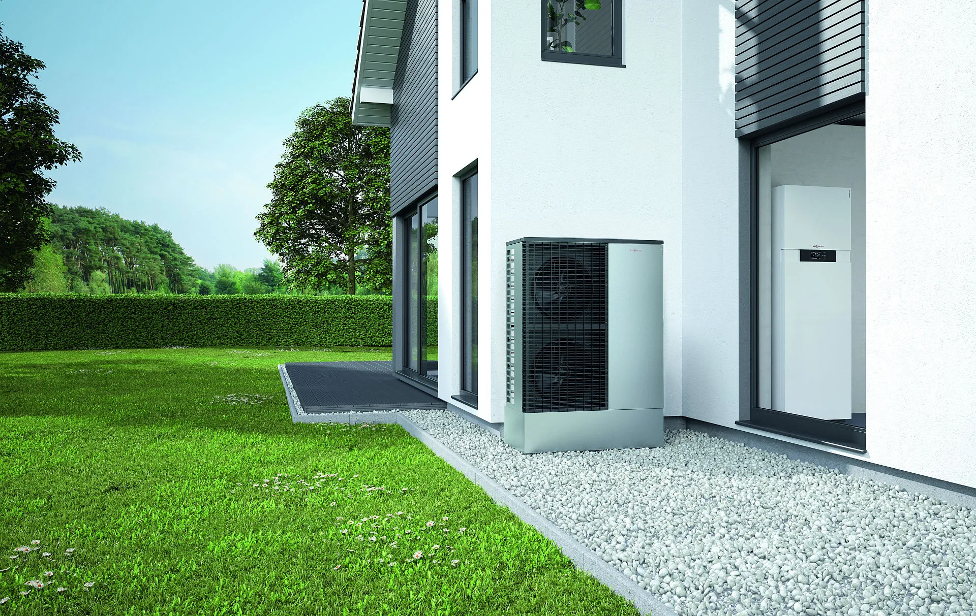 Eine kompakte Wärmepumpen-Außeneinheit ist neben einem Neubau installiert und ruht auf einem Metallständer über einem Kiesbett.