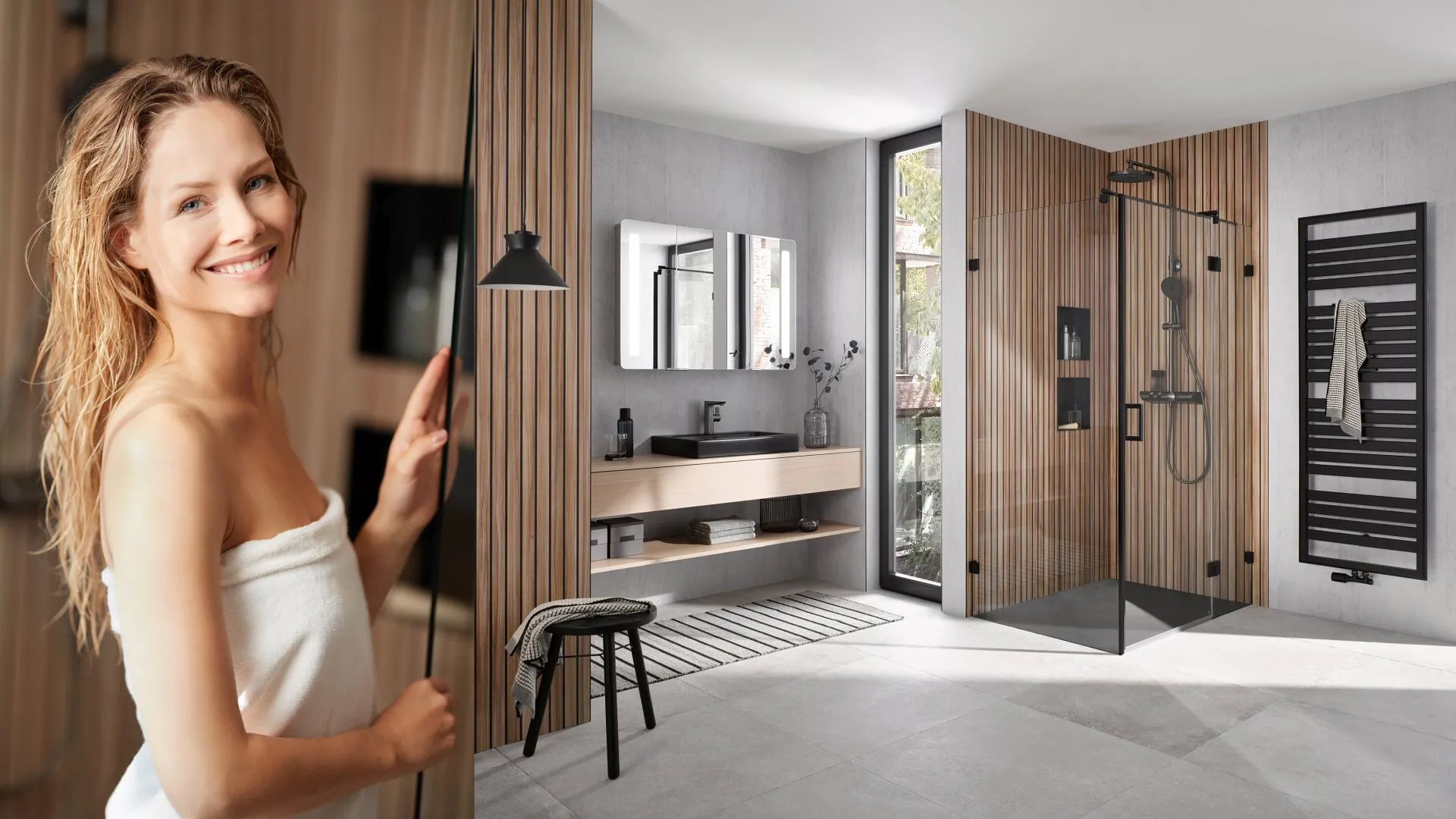 Frau im Wellness-Badezimmer vor moderner Walk-in-Dusche, Holzlamellen, Doppelspiegel und hellem Tageslicht.