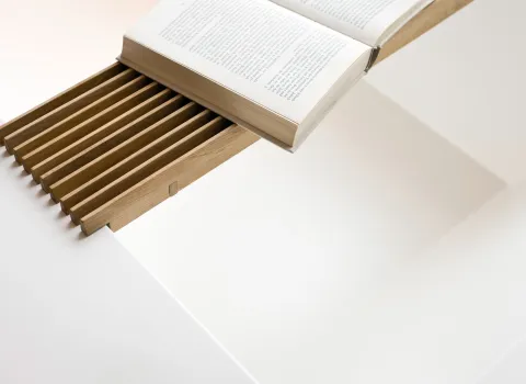 Ein aufgeschlagenes Buch liegt auf einer ausziehbaren Holzablage, die in einen weißen Tisch oder eine Fläche integriert ist.