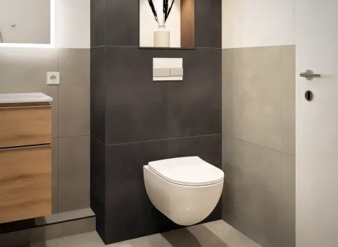 Minimalistisches Bad mit weißem wandmontiertem WC, Kontrastfliesen in Anthrazit und stilvoller Wandnische.
