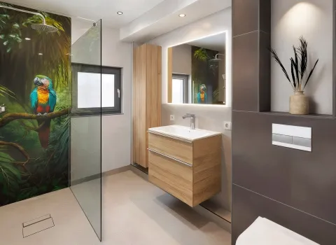 Ein modernes Badezimmer mit bodengleicher Dusche, deren Rückwand ein fotorealistisches Papageienmotiv im Dschungelstil zeigt. Der Waschtisch mit Holzfronten und der beleuchtete Spiegel sorgen für ein warmes, natürliches Ambiente. Eine dunkel geflieste WC-Vorwand mit dekorativer Nische bringt Struktur in den Raum. Spotlights und Tageslicht setzen gezielte Lichtakzente.