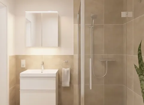 Ein kompaktes, modern eingerichtetes Badezimmer zeigt eine bodengleiche Dusche mit Glaswand und eine schwebende Waschtischanlage mit beleuchtetem Spiegelschrank. Die Wandfliesen in warmen Beigetönen verleihen dem Raum eine ruhige und natürliche Ausstrahlung. Ein Handtuchhalter mit weißem Handtuch hängt neben dem Waschbecken. Im rechten Vordergrund bringt eine grüne Pflanze Frische ins Design.