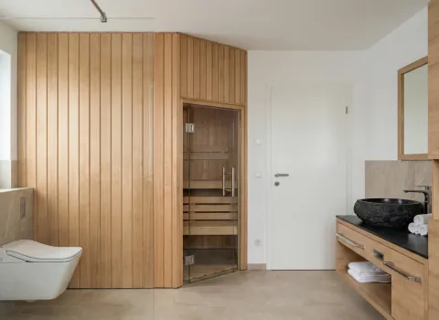 Badezimmer mit integrierter Holzsauna, wandhängendem WC und Naturstein-Waschbecken auf Waschtisch.