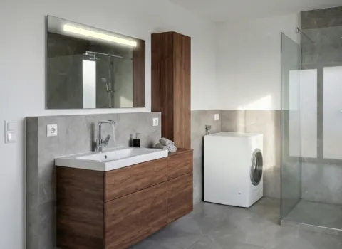 Stilvoll eingerichtetes Bad mit Waschtisch, Hochschrank, Waschmaschine und offener Dusche mit Glasverkleidung.