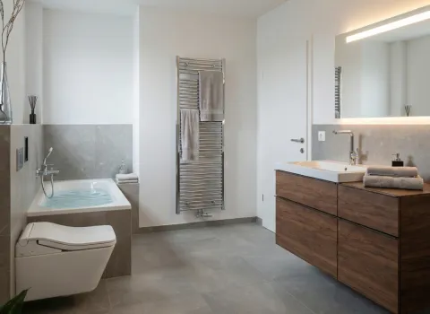 Hochwertiges Badezimmer mit Badewanne, wandhängender Toilette, stilvollem Waschtisch in Holzoptik und großem Spiegel mit LED-Beleuchtung.