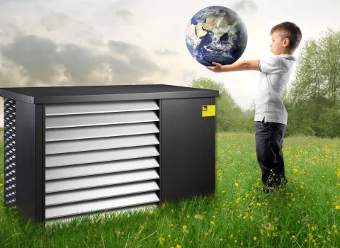 Eine Wärmepumpe von iDM seht auf einer Wiese neben einen Jungen, der einen Globus in beiden Händen hält, wie einen Ball.