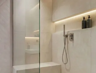 Moderne Walk-In-Dusche mit Glasabtrennung, integrierter Sitzbank und Regenduschkopf. Eine beleuchtete Nische bietet Platz für Duschgel und Shampoo.