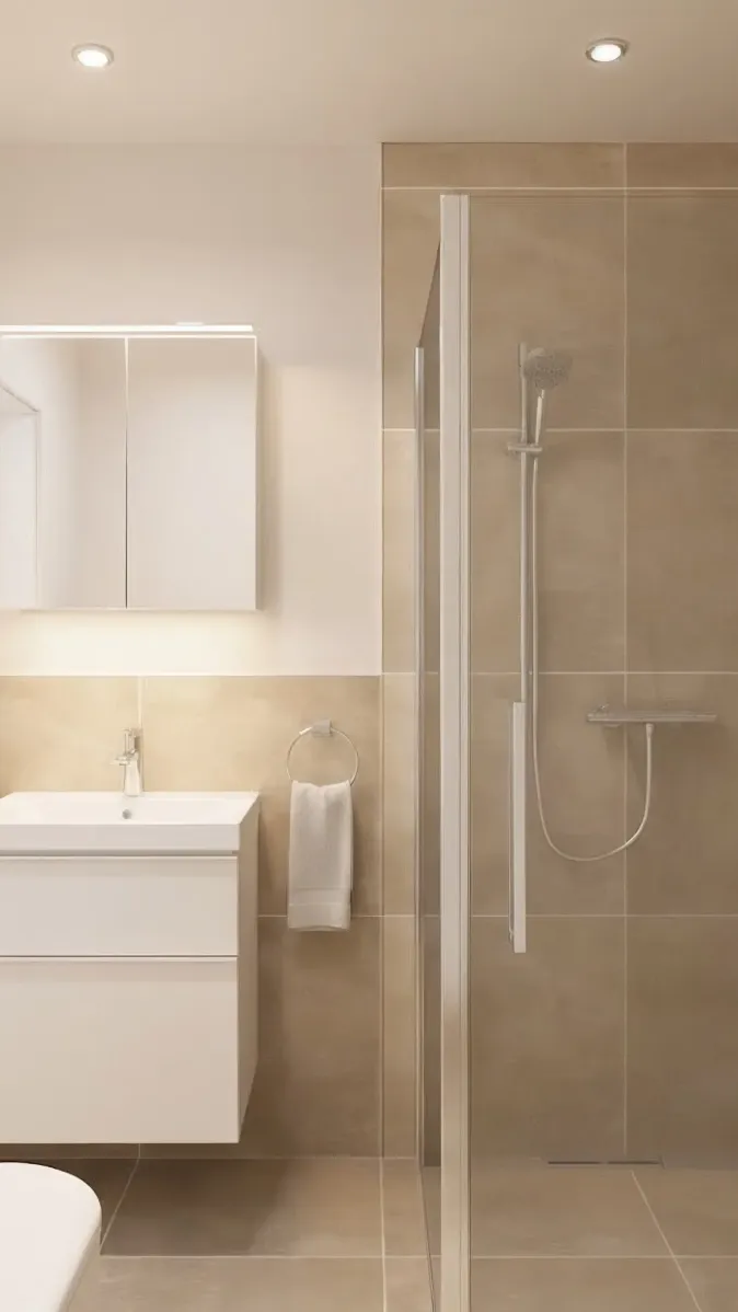 Ein kompaktes, modern eingerichtetes Badezimmer zeigt eine bodengleiche Dusche mit Glaswand und eine schwebende Waschtischanlage mit beleuchtetem Spiegelschrank. Die Wandfliesen in warmen Beigetönen verleihen dem Raum eine ruhige und natürliche Ausstrahlung. Ein Handtuchhalter mit weißem Handtuch hängt neben dem Waschbecken. Im rechten Vordergrund bringt eine grüne Pflanze Frische ins Design.