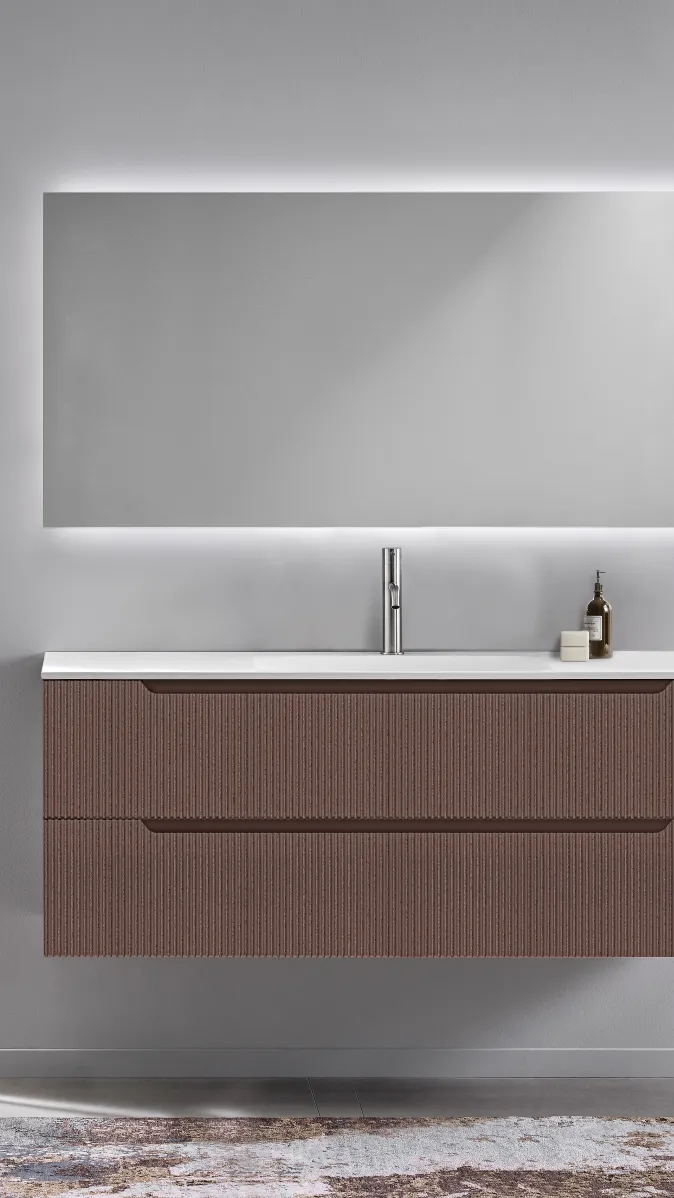 Wandhängendes Badmöbel mit geriffelter Front in Terracotta und großem beleuchtetem Spiegel.